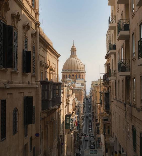 A street view in Valletta, Malta, with a clear view of the dome of the Basilica of Our Lady of Mount Carmel.